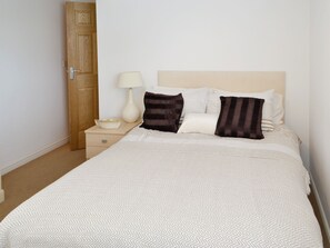 Cama bem arrumada com colcha estampada, dois travesseiros, luminária de cabeceira e porta de madeira.