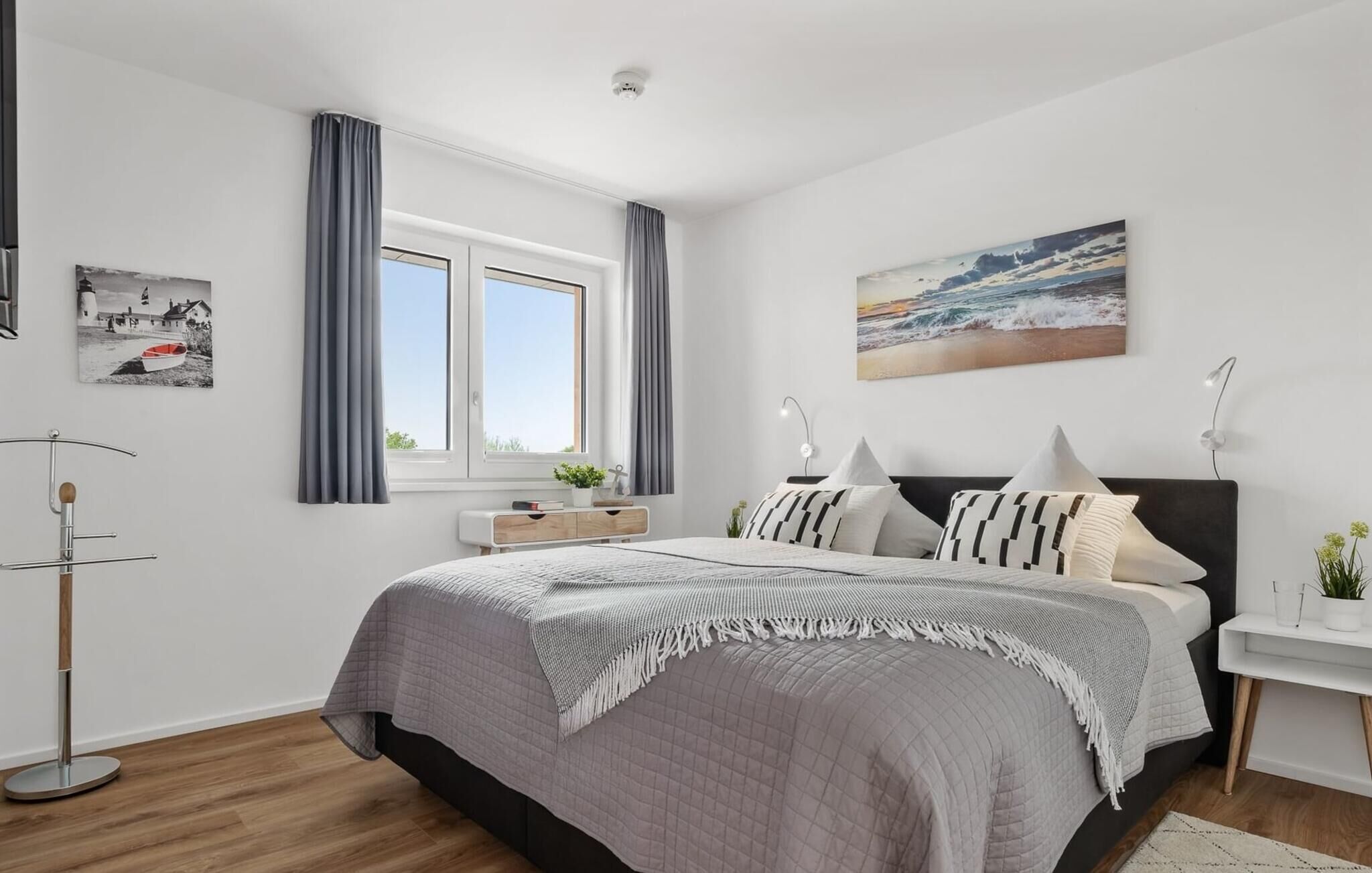 Una camera da letto moderna con un letto grande, una finestra con tende, un comodino con una lampada e opere d'arte alle pareti.