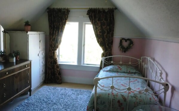 A bedroom with a bed, a dresser, a window with curtains, and a heart-shaped decoration on the wall. - Charming James Bay Guesthouse by Fisherman's Wharf (Victoria)