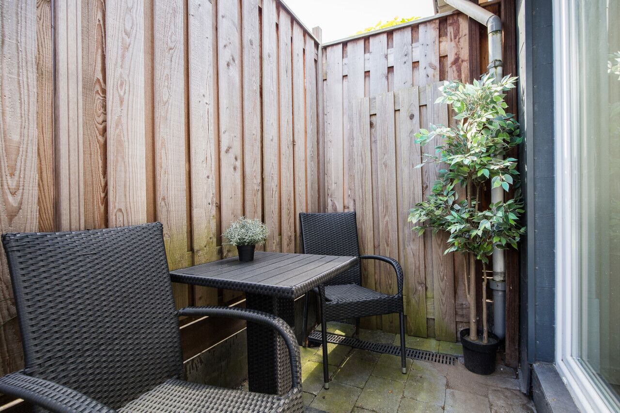 Un patio con valla de madera, una mesa, dos sillas y una planta en maceta.