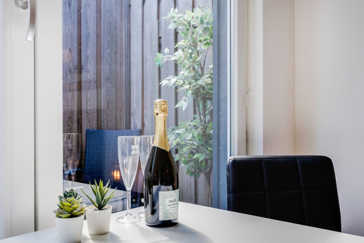 Un tavolo con una bottiglia di champagne Mezza, due bicchieri e due piante in vaso.