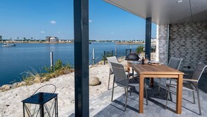 An outdoor dining area with a view of a lake and boats, featuring a table with chairs and a grill. - Lovely apartment in Olpenitz with sauna (Olpenitz)