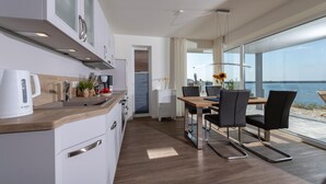 A modern kitchen with a wooden countertop, white cabinets, and a Bosch coffee maker. There is a dining area with a wooden table and black chairs, and a large window offering a view of the sea. - Lovely apartment in Olpenitz with sauna (Olpenitz)