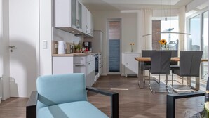 A modern kitchen with white cabinets and a dining area with a table and chairs. - Lovely apartment in Olpenitz with sauna (Olpenitz)