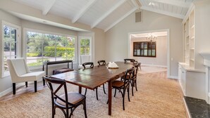 A spacious dining area with a long wooden table, several chairs, and a bench. Large windows provide natural light and views of greenery outside. - Large Quiet Sonoma Oasis with Pool (Sonoma)