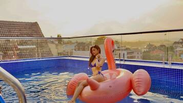 Uma pessoa sentada em um flamingue rosa inflável em uma piscina, com vista para casas ao fundo.