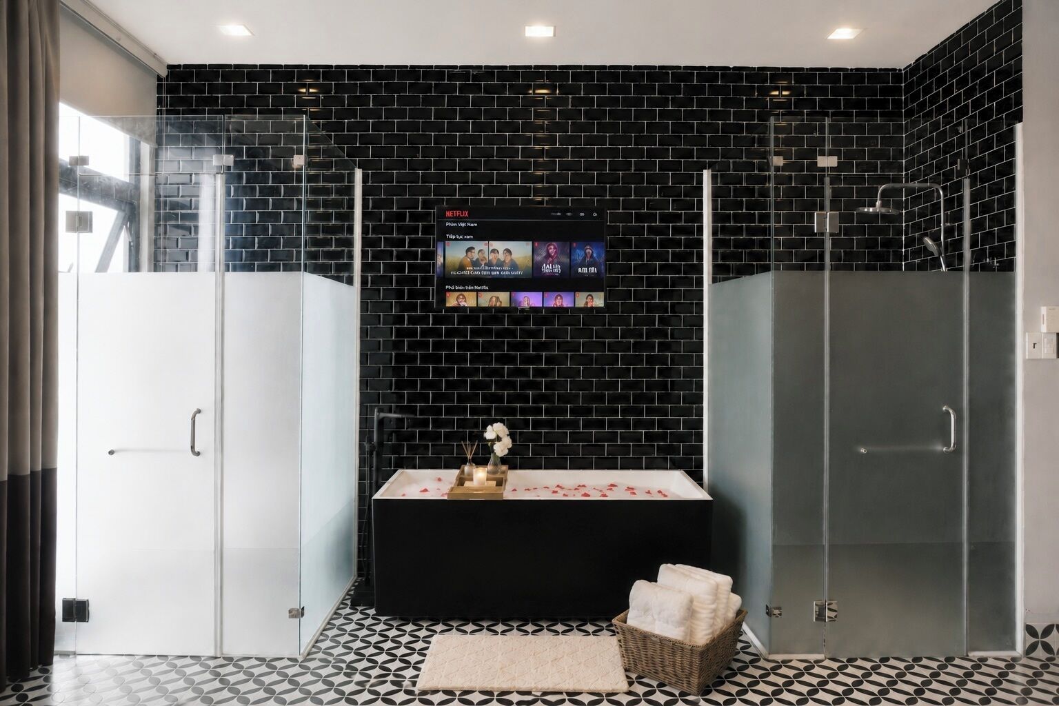 Un bagno moderno con una parete rivestita in piastrelle nere, un box doccia in vetro, un lavabo bianco con vassoio e un pavimento decorato.