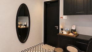 Une chambre d’hôtel avec une porte noire, un miroir, une petite table sur laquelle se trouve un plateau avec divers objets, et un sol à motifs.