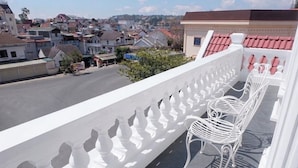Un balcon doté de balustrades blanches et de chaises, donnant sur un quartier résidentiel avec des maisons et un ciel dégagé.