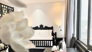 Ein Hotelzimmer mit einem Bett, einem Tisch mit Teekanne, einem Sessel und Blick durch große Fenster nach draußen.