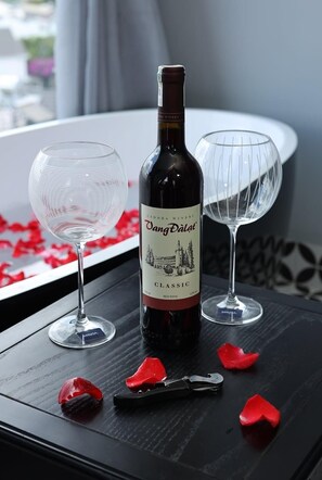 A bottle of wine, two wine glasses, and a wine opener on a table with red rose petals. - TTR Skypool View Hotel (Da Lat)