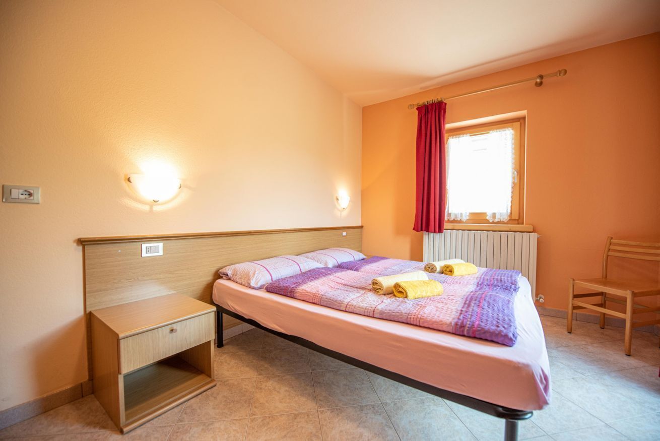 Un lit simple avec une tête de lit, une table de chevet, une fenêtre avec des rideaux et un radiateur.