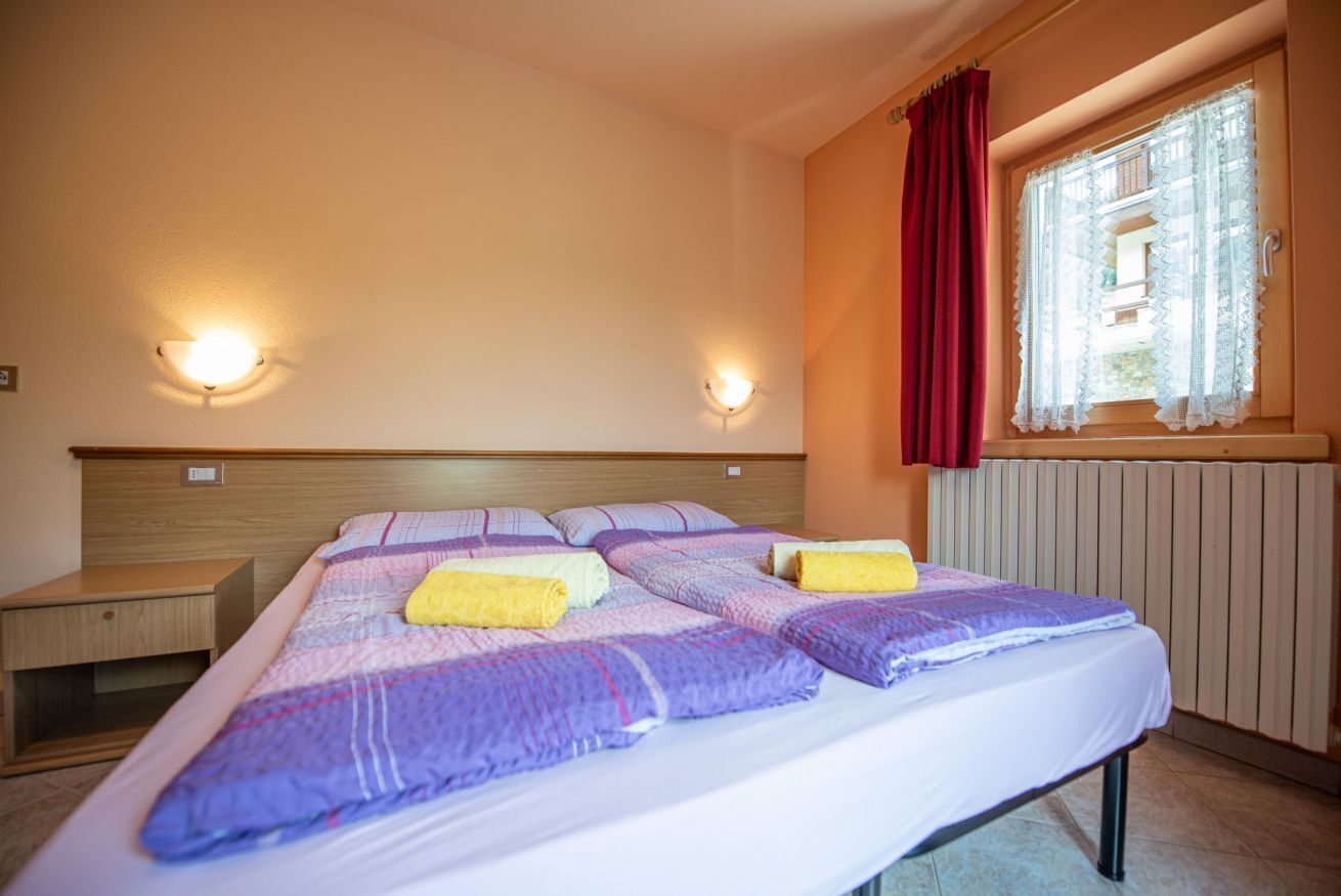 Quarto com cama, duas mesas de cabeceira, janela com cortinas e luminárias na parede.