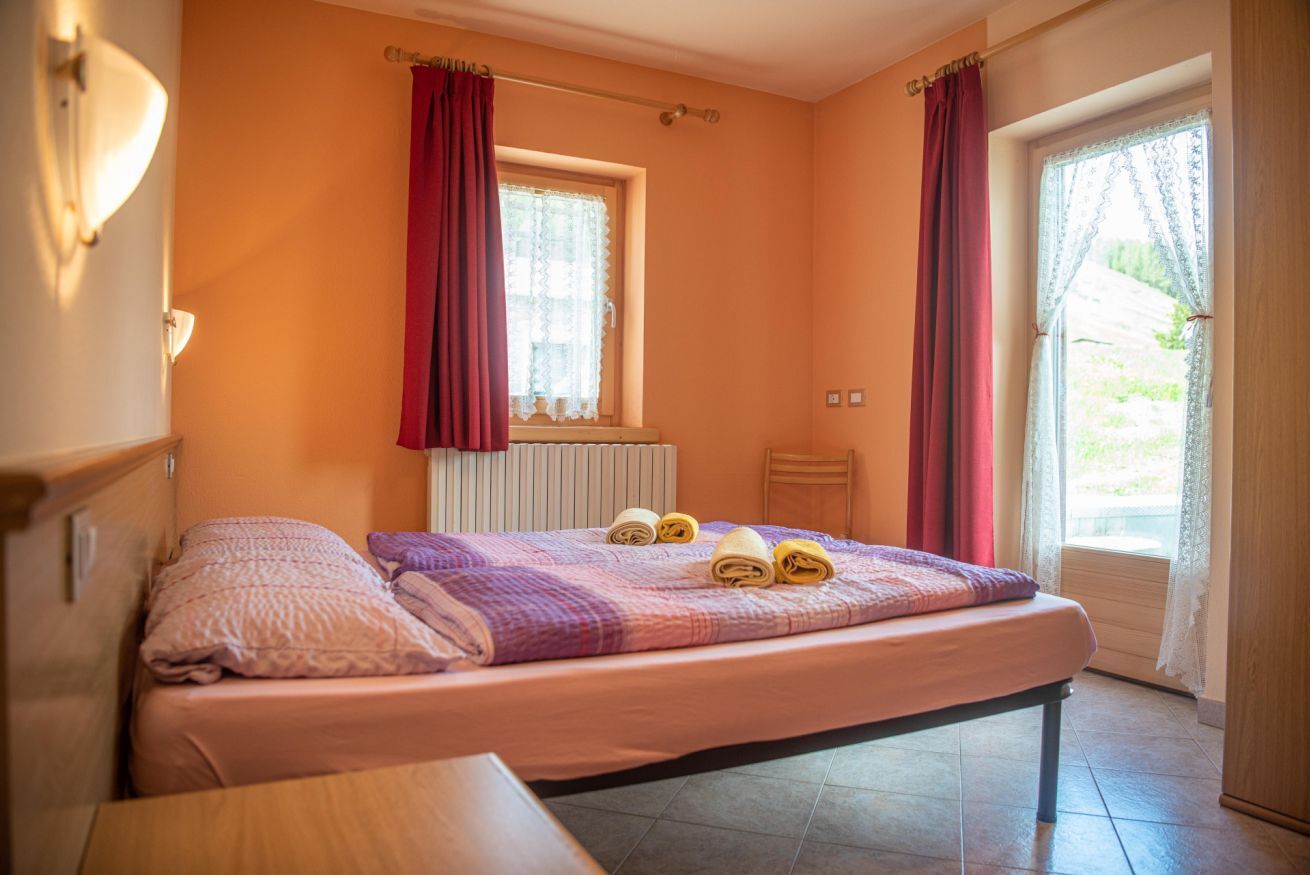 Ein Schlafzimmer mit Bett, einem fenster mit Vorhängen, einer Heizung und einer Tür, die nach draußen führt.