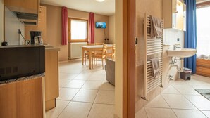 Een kleine keuken met een televisie, een eethoek met stoelen, en een badkamer met een wastafel en handdoekhouder.