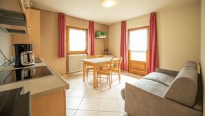 Een kleine keuken met een eettafel en stoelen, een bank en een aan de muur bevestigde televisie.
