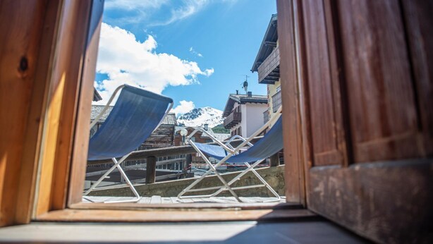A view through a window of a room with two blue lounge chairs and a wooden floor. - Be won over by the Valente two-room apartment and enjoy your vacation (Livigno)