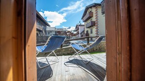 A wooden deck with two blue lounge chairs, a stone wall, and buildings in the background. - Be won over by the Valente two-room apartment and enjoy your vacation (Livigno)
