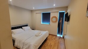 Une chambre à coucher avec un lit, une fenêtre, un téléviseur fixé au mur et une porte.