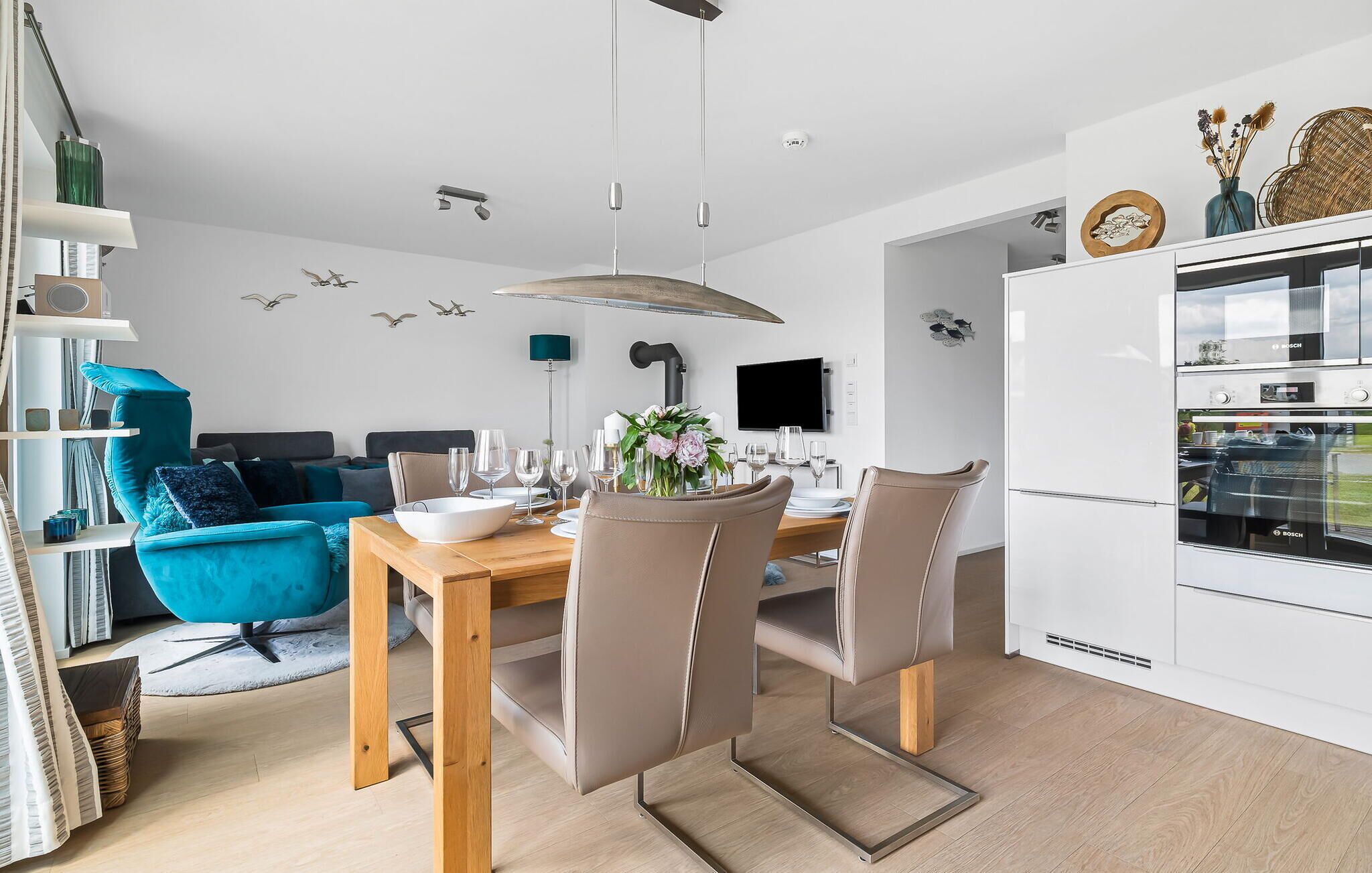 Eine moderne Küche mit einem Bosch-Kühlschrank, ein Essbereich mit einem Holztisch und -stühlen sowie ein smaragdgrünes Sofa im Wohnbereich.