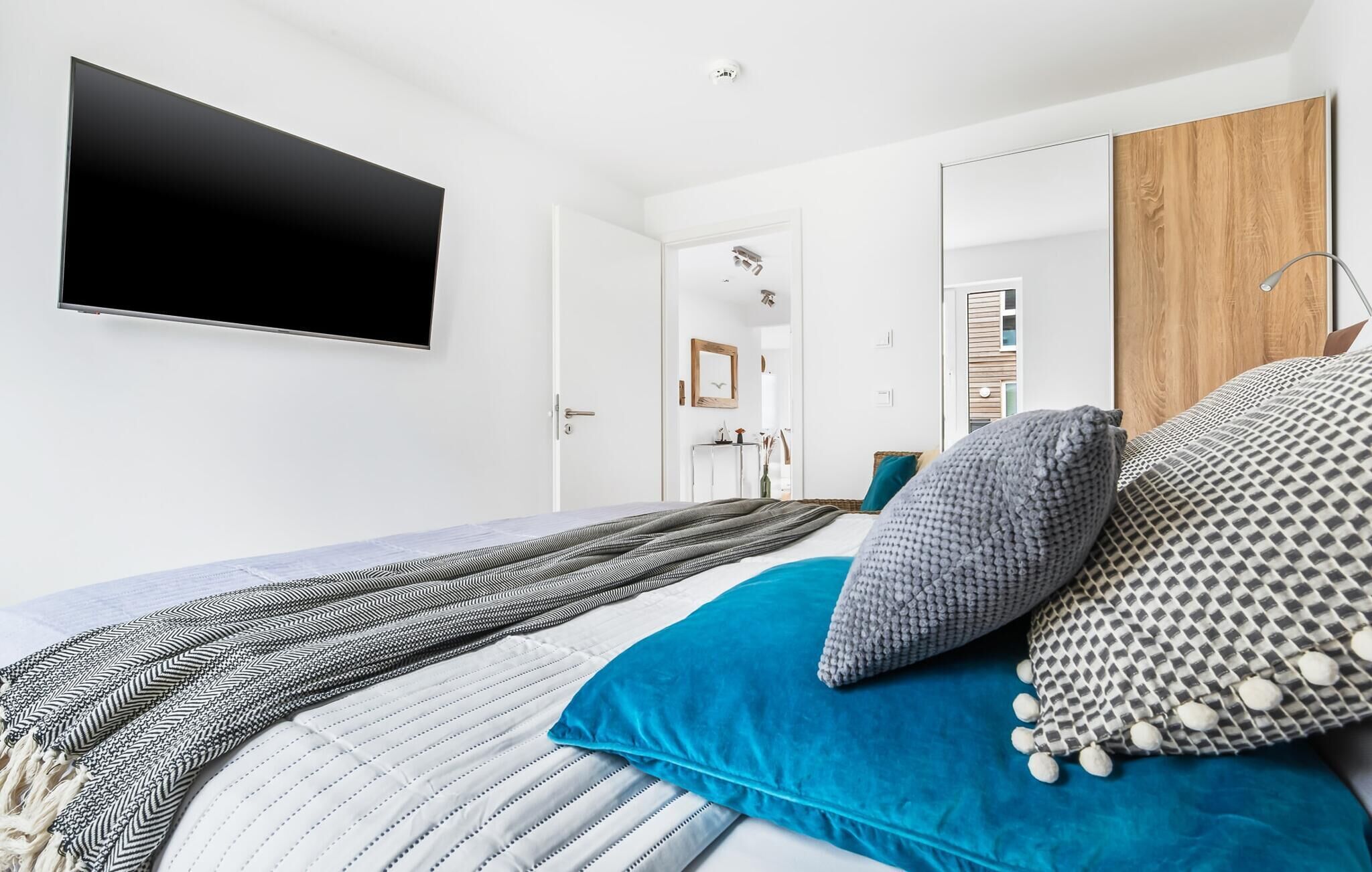 A modern bedroom with a large bed, a flat-screen TV mounted on the wall, and a wooden wardrobe.