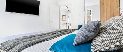 A modern bedroom with a large bed, a flat-screen TV mounted on the wall, and a wooden wardrobe.