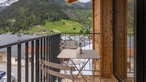 A wooden balcony with a table and chairs, overlooking a mountainous landscape and a body of water. - MAISON ORIGINE - BEAUFORT (BEAUFORT)