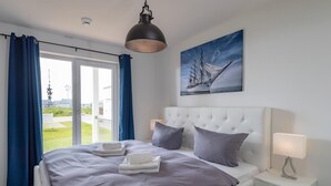 A bedroom with a large bed, a headboard, a nightstand, a lamp, and a painting of a ship on the wall. - Beautiful apartment in Olpenitz (Olpenitz)