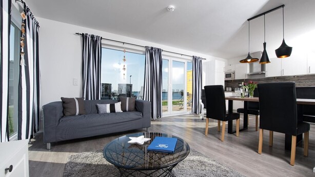 A modern living room with a sofa, a glass coffee table, and a dining area with chairs and a table. - Beautiful apartment in Olpenitz (Olpenitz)