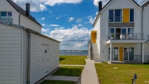 A residential area with two white houses, one with a yellow accent, a paved walkway, and a grassy lawn. - Beautiful apartment in Olpenitz (Olpenitz)