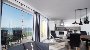 A modern apartment with a balcony overlooking a body of water, a dining area, and a kitchen. - Beautiful apartment in Olpenitz (Olpenitz)