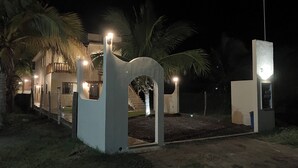 A modern house with a well-lit entrance, palm trees, and a staircase leading to the upper floor. - Los Amores Apartments C (Perula)