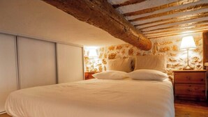 Ein Schlafzimmer mit einem großen Bett, Holzbalken an der Decke, einem Nachttisch mit Lampe und einer Wand mit floralem Muster.