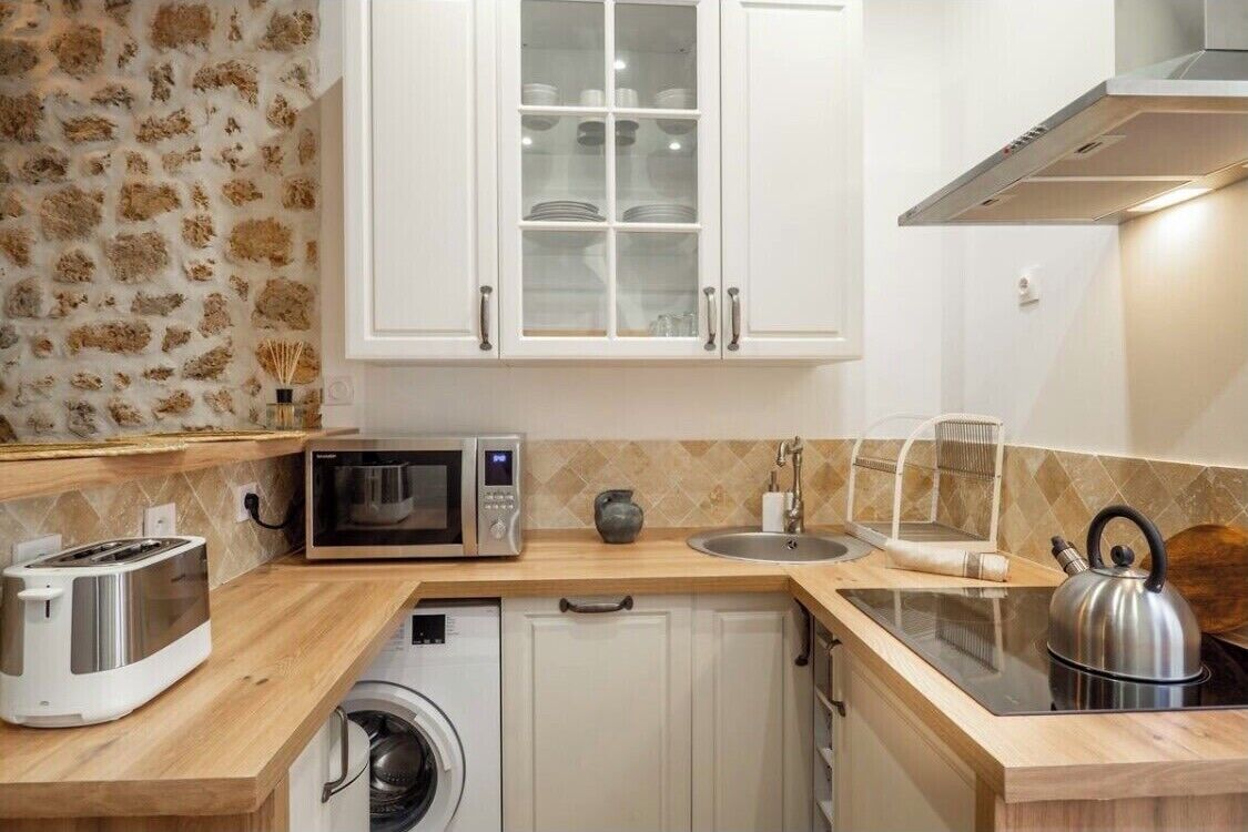 A compact kitchen with white cabinets, a microwave, a toaster, a kettle, and a washing machine.