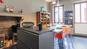 Une cuisine moderne dotée d’un îlot central, d’étagères en bois et d’un coin repas avec des chaises orange.