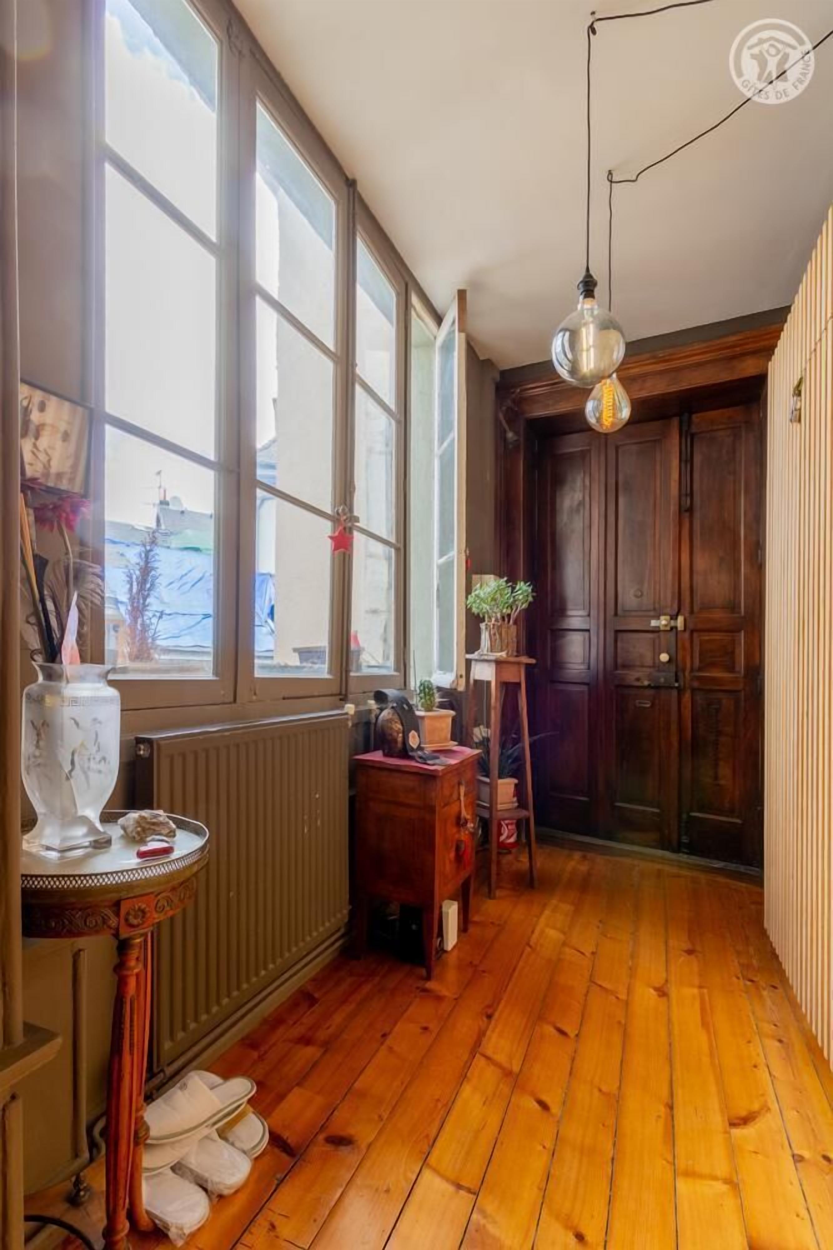 Un couloir doté d’un plancher en bois, de grandes fenêtres, d’un radiateur et d’une porte.