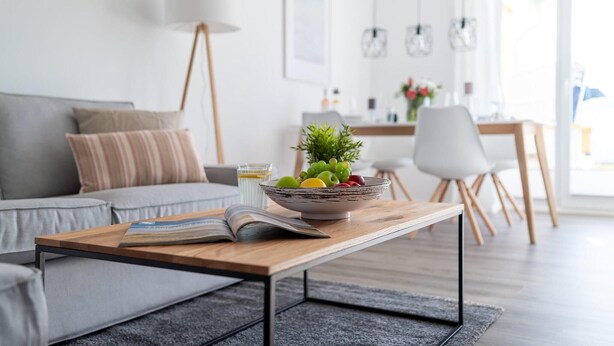 Een moderne woonkamer met een grijze bank, een houten salontafel met een schaal fruit en een tijdschrift.