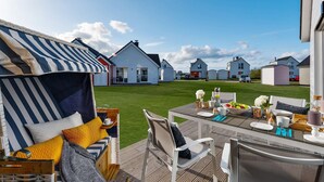 Een terras met buitenmeubelen, een gestreept zonnescherm en een uitzicht op witte huizen op de achtergrond.