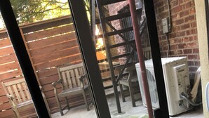 Une vue à travers une fenêtre donnant sur un patio, avec une clôture en bois, du mobilier d’extérieur et un mur en briques.