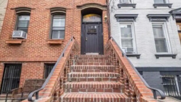 Un bâtiment en briques avec une porte noire et un escalier menant à l’entrée.