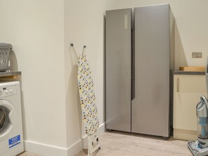 A compact kitchen with a washing machine, a polka-dotted ironing board, and a stainless steel refrigerator.