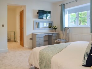 Een slaapkamer met een bed, een dressoir, een televisie, een raam en een deur.
