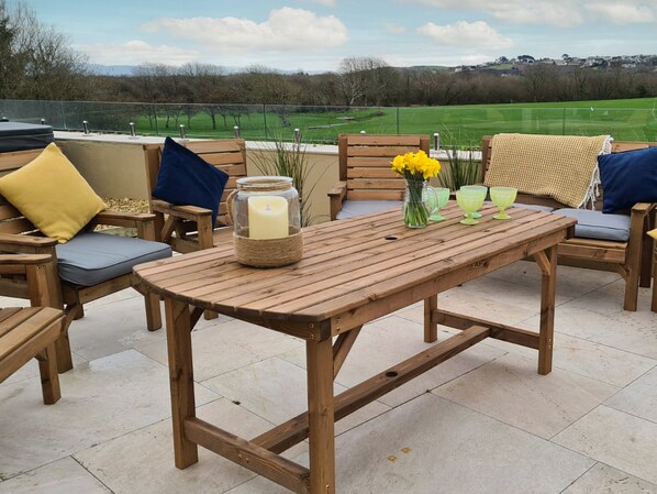 Un patio al aire libre con muebles de madera, una mesa con una vela y un florero con flores amarillas.