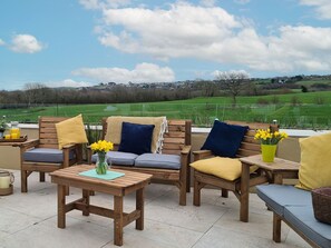 Een terras met houten meubels, kussens en uitzicht op een groen veld.