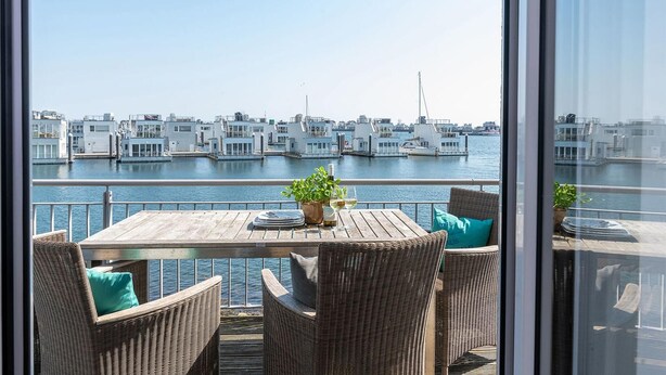 A balcony with wicker furniture, a table with a bottle and glass, and a view of a marina with boats.