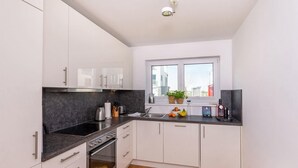 A modern kitchen with white cabinets, a black countertop, a stove, and a window with plants.
