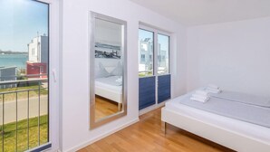 A modern bedroom with a large window, a bed, and a view of the sea.