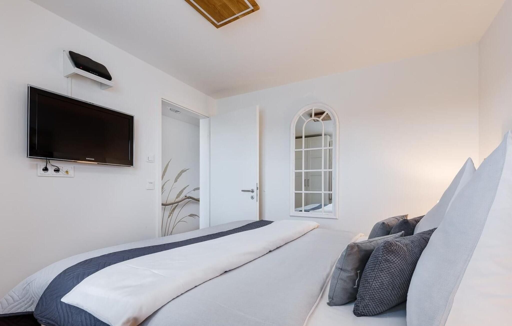 Un dormitorio con una cama, un televisor de pantalla plana en la pared, una puerta y una ventana.