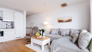 Una sala de estar moderna con un sofá gris, una mesa de centro y un comedor con armarios blancos y una cafetera.