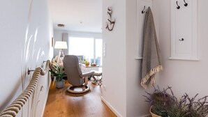 Un pasillo con suelo de madera, una silla, una lámpara y una planta.